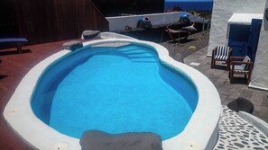Una piscina de borde curvo, rodeada por una zona de patio con sillas y una mesa.
