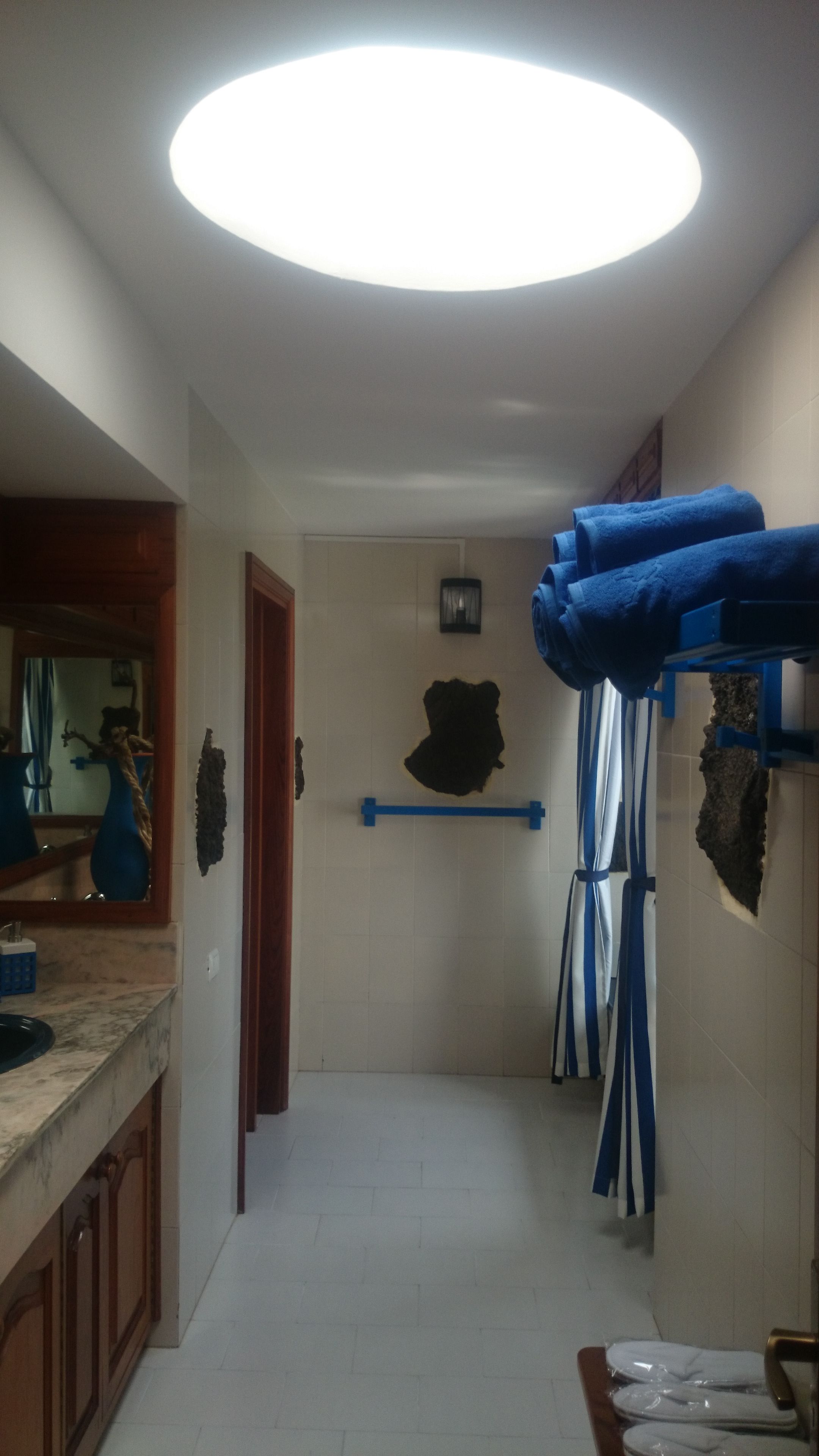 Un baño con techo blanco, toallero azul y un espejo.