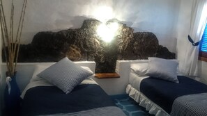 Una habitación con dos camas, una pared de roca y una ventana con persianas.