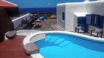 Zona de piscina con vista al océano, una silla de descanso y una mesita.