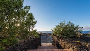 A pathway leading to a beach with a metal gate, surrounded by vegetation and a clear sky. - Villa Juan (Frontera)
