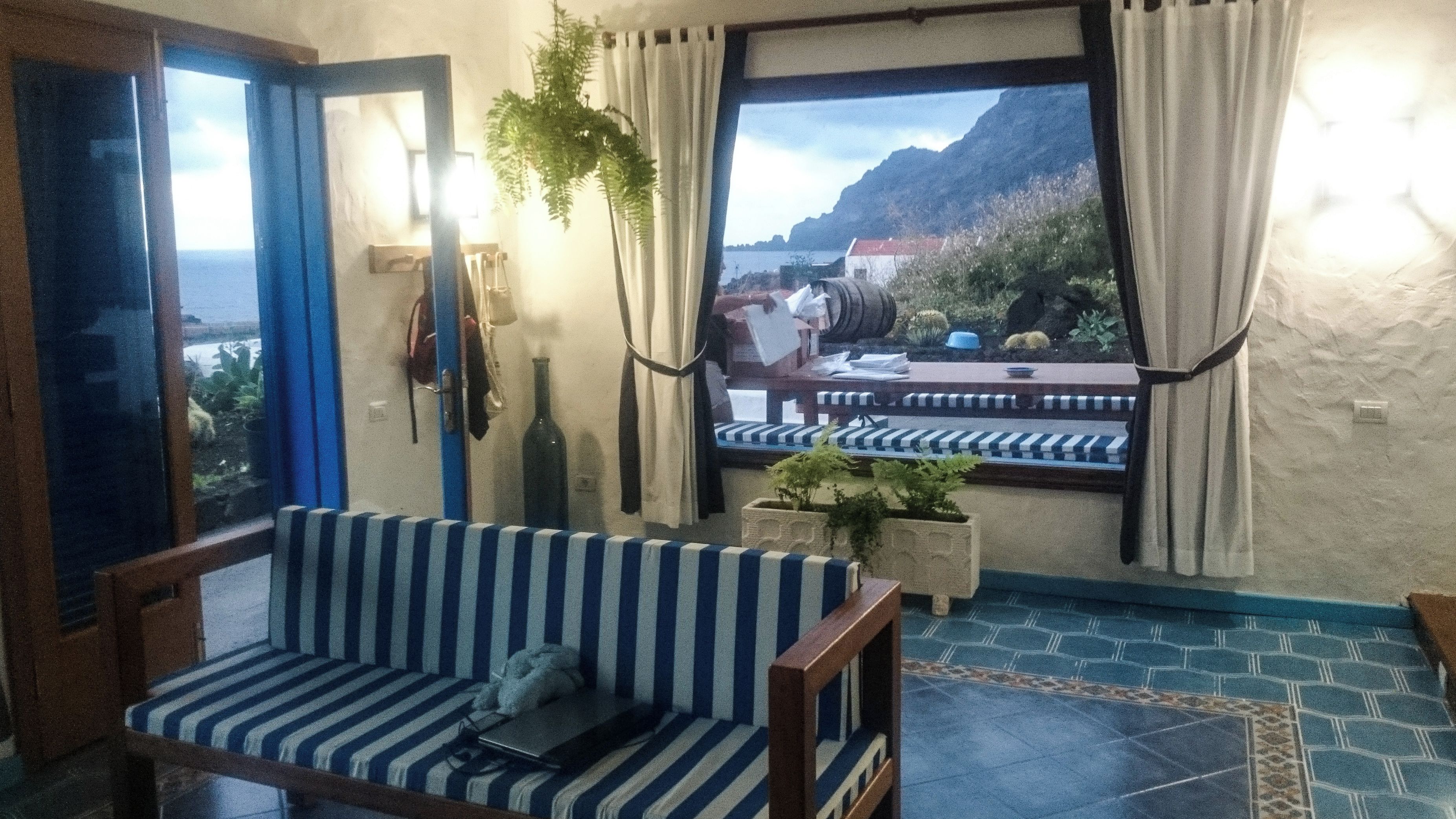 Une pièce avec un canapé à rayures, une petite table, une fenêtre avec des rideaux et une vue sur un paysage montagneux.