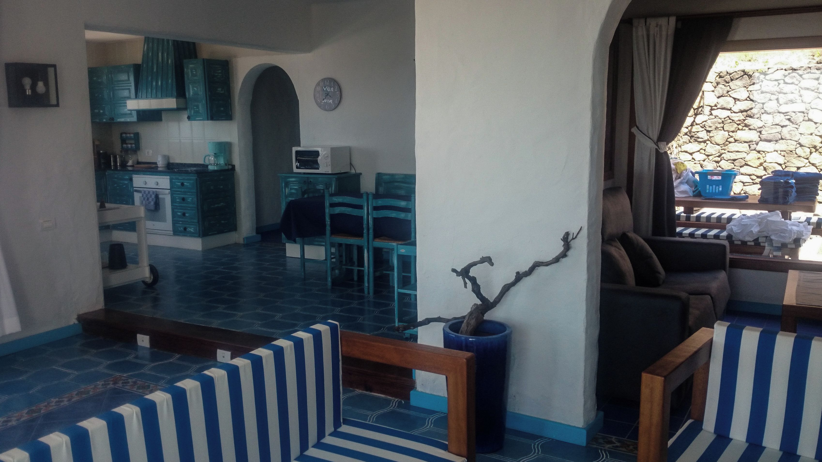 A living area with a sofa set, a dining table with chairs, a kitchen area, and a stone wall outside.