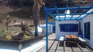 Un espacio de estar al aire libre cubierto con una mesa y bancos de madera, una pérgola azul y vistas a un paisaje montañoso.