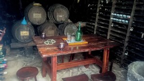 A rustic wooden table with a bottle and glasses, surrounded by barrels in a dimly lit cellar. - Villa Juan (Frontera)