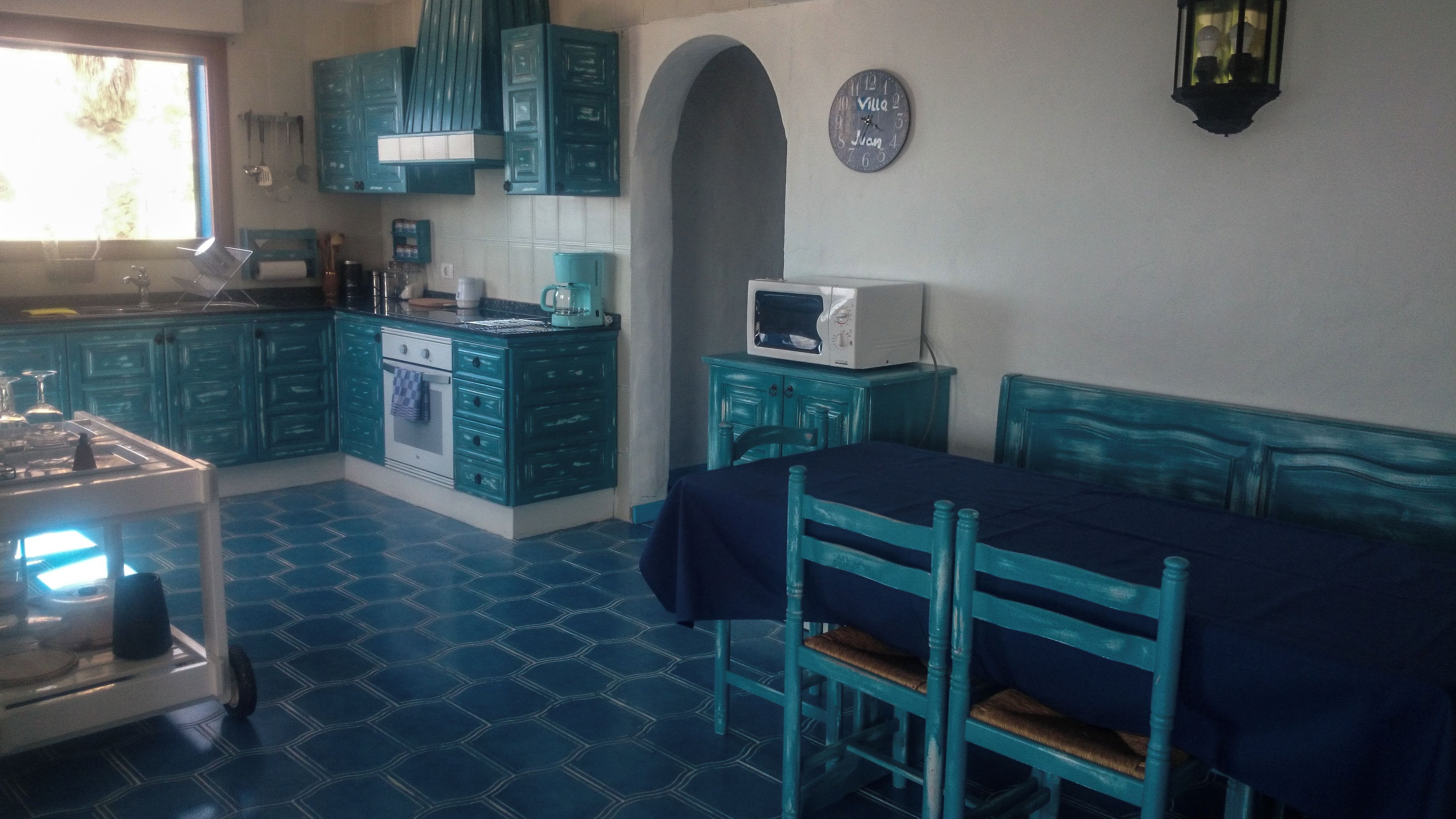 A kitchen with teal cabinetry, a microwave, and a dining area with a table and chairs.