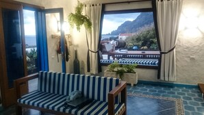 A room with a striped sofa, a small table, a window with curtains, and a view of mountains and a body of water. - Villa Juan (Frontera)