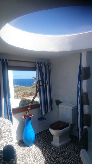 Un baño con inodoro, un jarrón azul y vistas al mar.