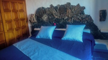Una cama con ropa de cama azul y almohadas a rayas, un armario de madera y una pared de piedra detrás de la cama.