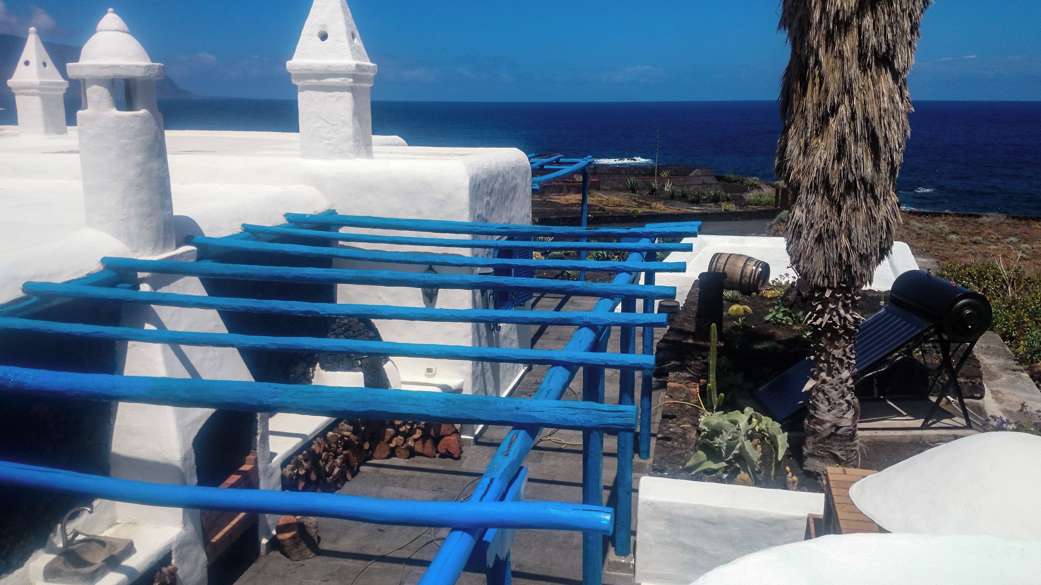 A coastal building with white walls and blue railings, overlooking the sea.