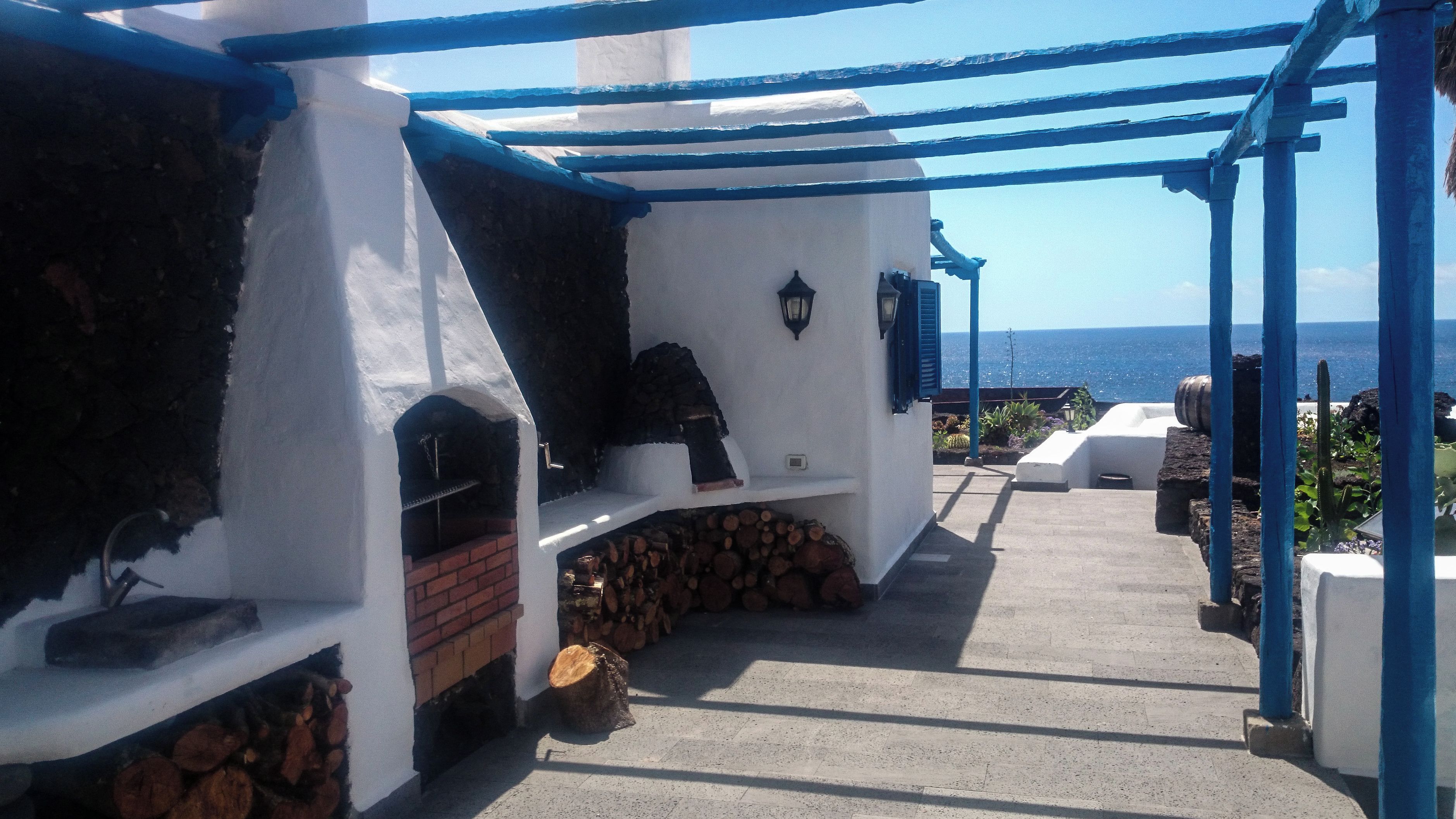 Un espacio al aire libre techado con una parrilla, un horno de ladrillo y vistas al mar.