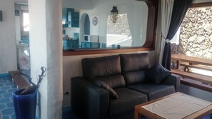 Una sala de estar con un sofá de cuero, una mesa de madera y vista a la cocina por una ventana.