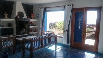 Una sala de estar con chimenea, una mesa de comedor, sillas y vistas al exterior a través de un ventanal.