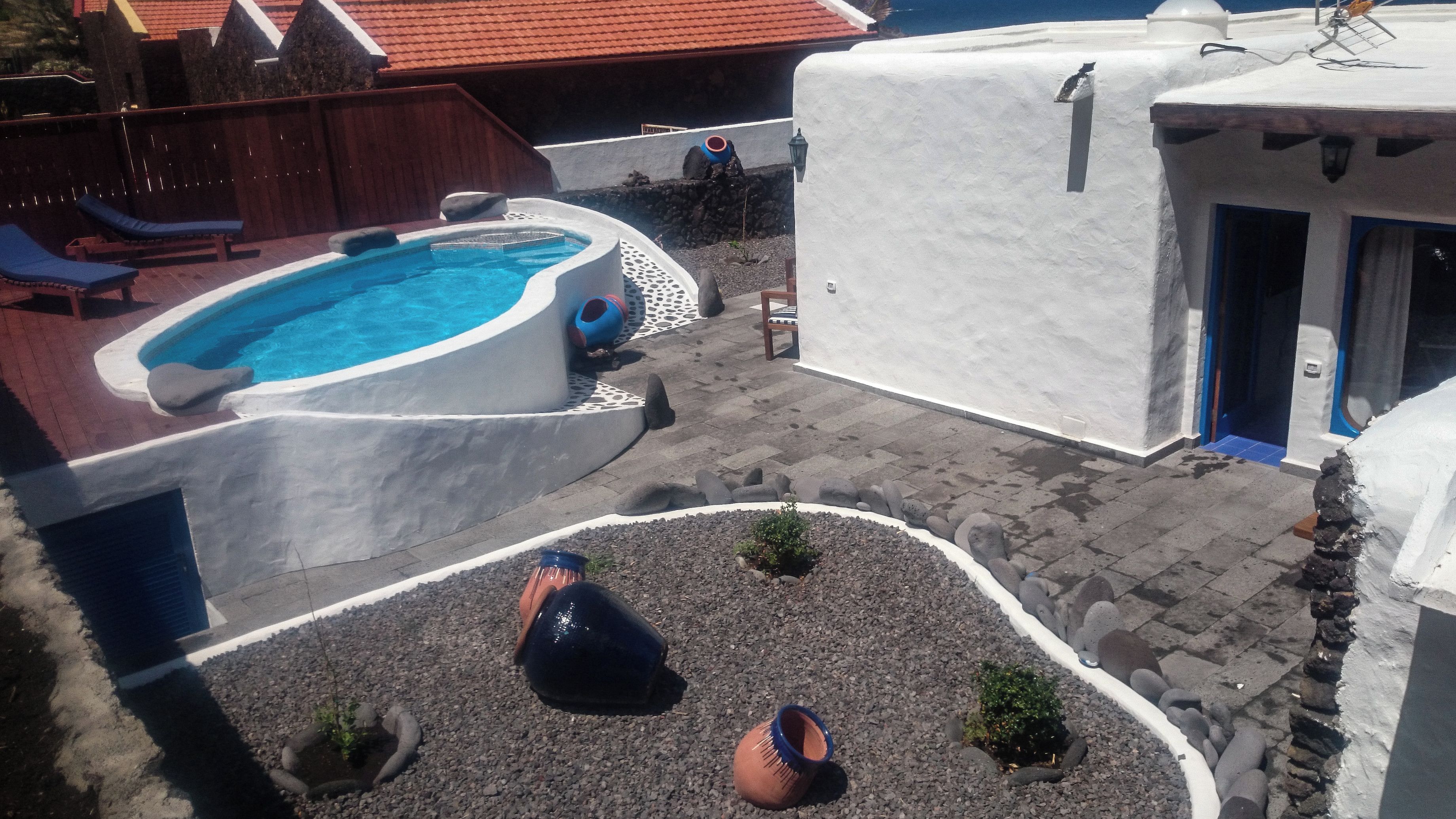 A swimming pool with a hot tub, surrounded by a white wall and a stone pathway.