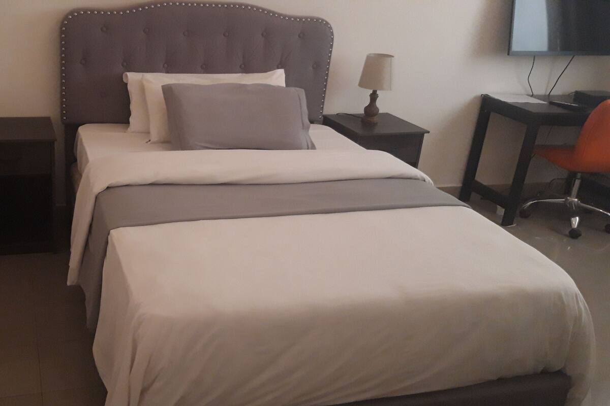 Un lit bien fait, avec une tête de lit, une table de chevet avec une lampe et une chaise.