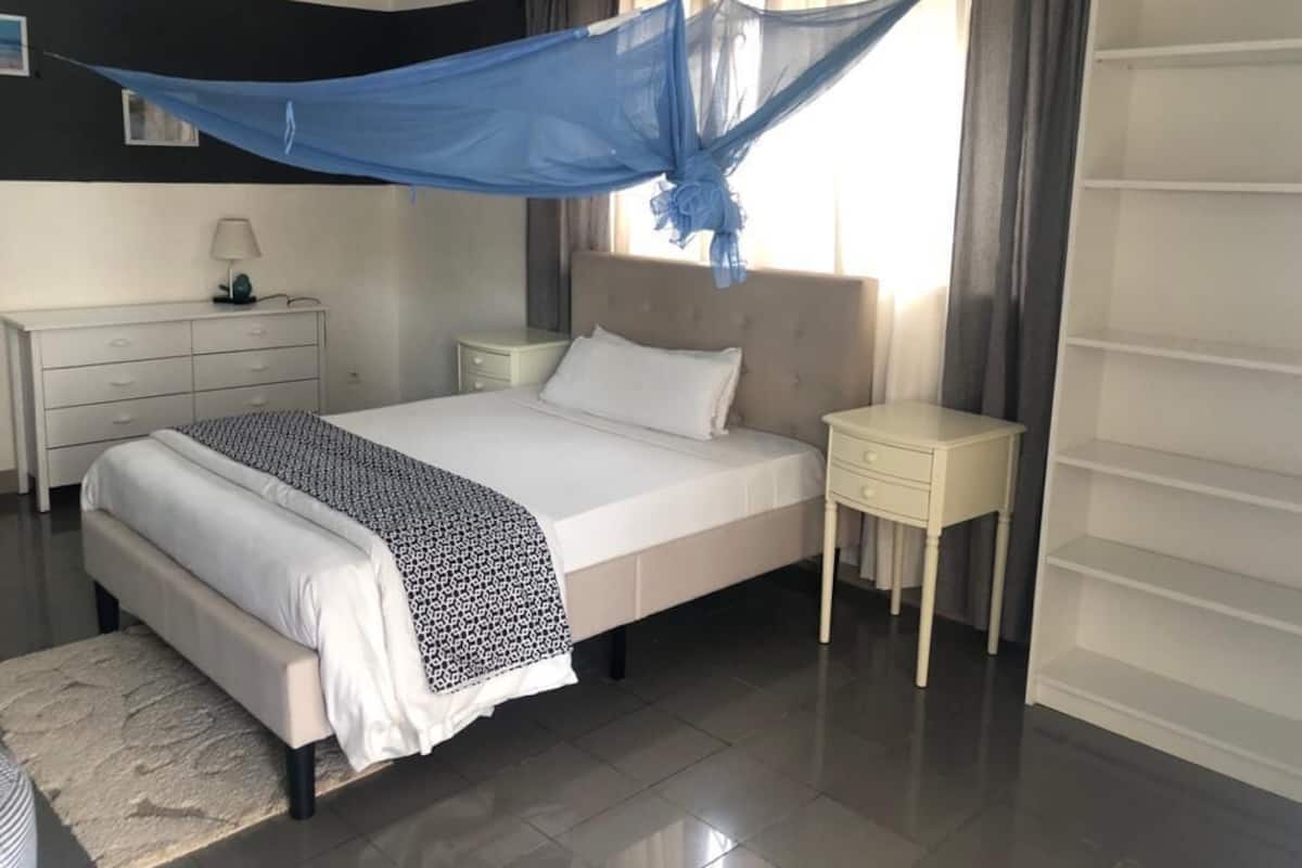 Une chambre à coucher comprenant un lit, des tables de chevet, une commode, une armoire et une fenêtre avec des rideaux.