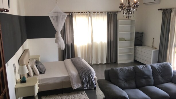 A bedroom with a bed, bedside table, lamp, and a large window with curtains. - Hotel Le Littoral des Almadies (Dakar)