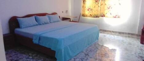 A bedroom with a bed, a nightstand, a window with floral curtains, and a marble floor.