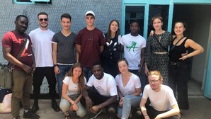 A group of people posing in front of a building with a textured wall and a blue door. - Sweet Stay Guest House (Kigali)