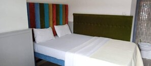 A bed with a green headboard, white bedding, and colorful striped curtains. - Sweet Stay Guest House (Kigali)