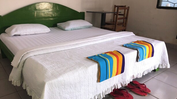 A bed with a white quilt and a colorful striped blanket, a green headboard, and a wooden chair beside it. - Sweet Stay Guest House (Kigali)