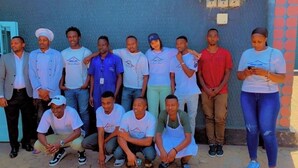 A group of people standing and sitting in front of a building with a blue wall and a door. - Sweet Stay Guest House (Kigali)