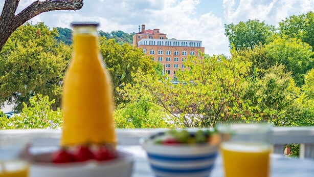 Ein Esstisch mit einer Flasche, einer Schüssel und Gläsern, mit Blick auf ein Gebäude und Bäume.
