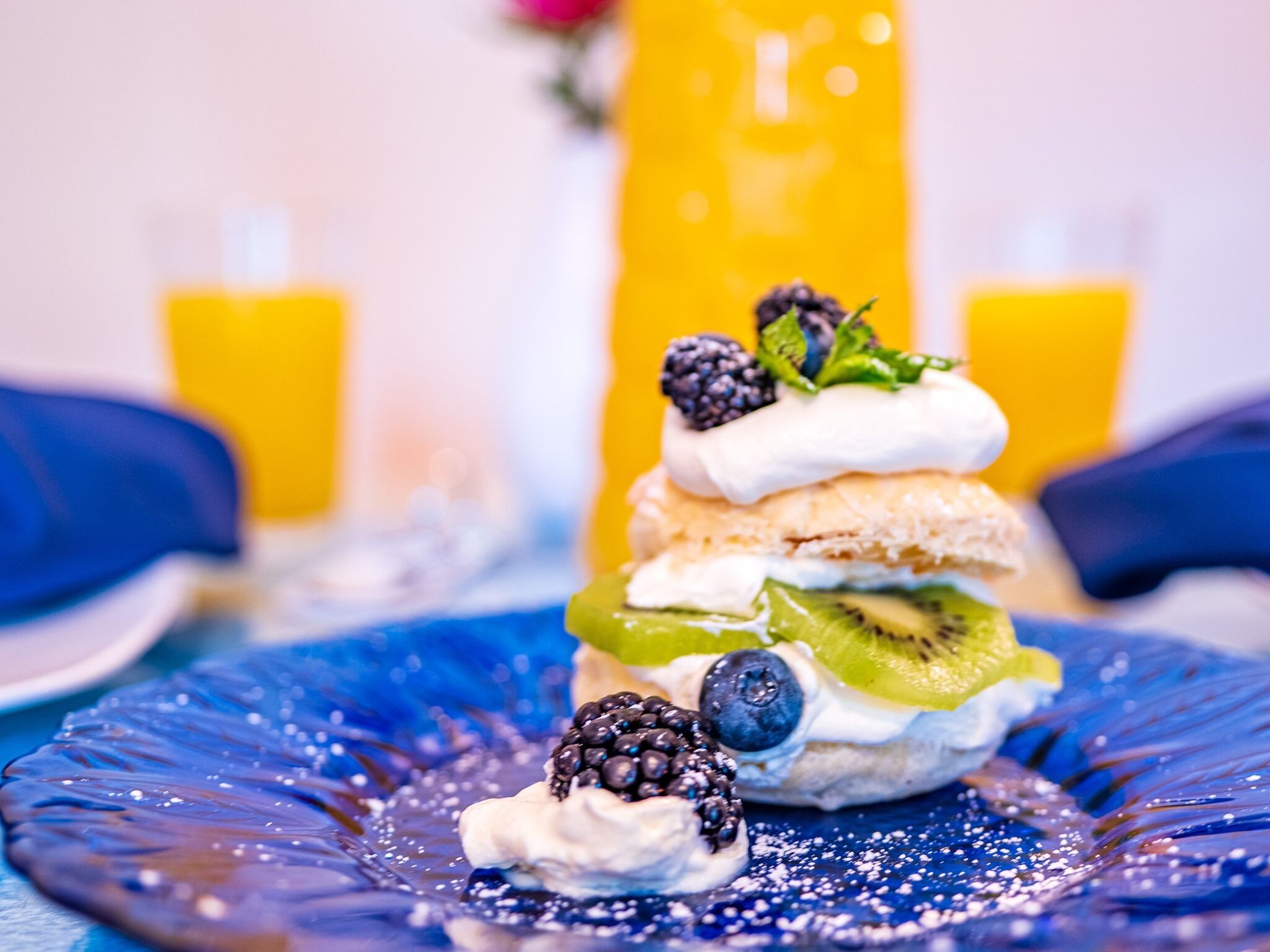 Sobremesa em um prato azul com chantilly, frutas vermelhas e uma fatia de kiwi.