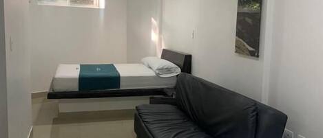 A hotel room with a bed, a sofa, a small table, and a poster on the wall.