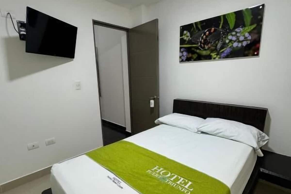 A hotel room with a bed, a flat-screen TV mounted on the wall, a door, and a framed picture of flowers.