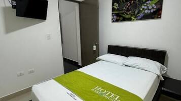 Habitación de hotel con cama, televisor de pantalla plana montado en la pared, una puerta y un cuadro con flores.