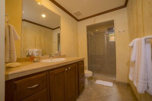 A bathroom with a sink, mirror, wooden cabinets, a toilet, and a shower. - Los Suenos Resort Veranda 8F (Jacó)