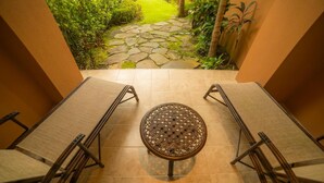 A patio area with a round table and four chairs, a stone pathway leading to a garden, and a view of greenery. - Los Suenos Resort Veranda 8F (Jacó)