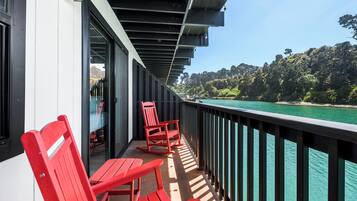 A balcony with red chairs, a table, and a view of a forested coastline.