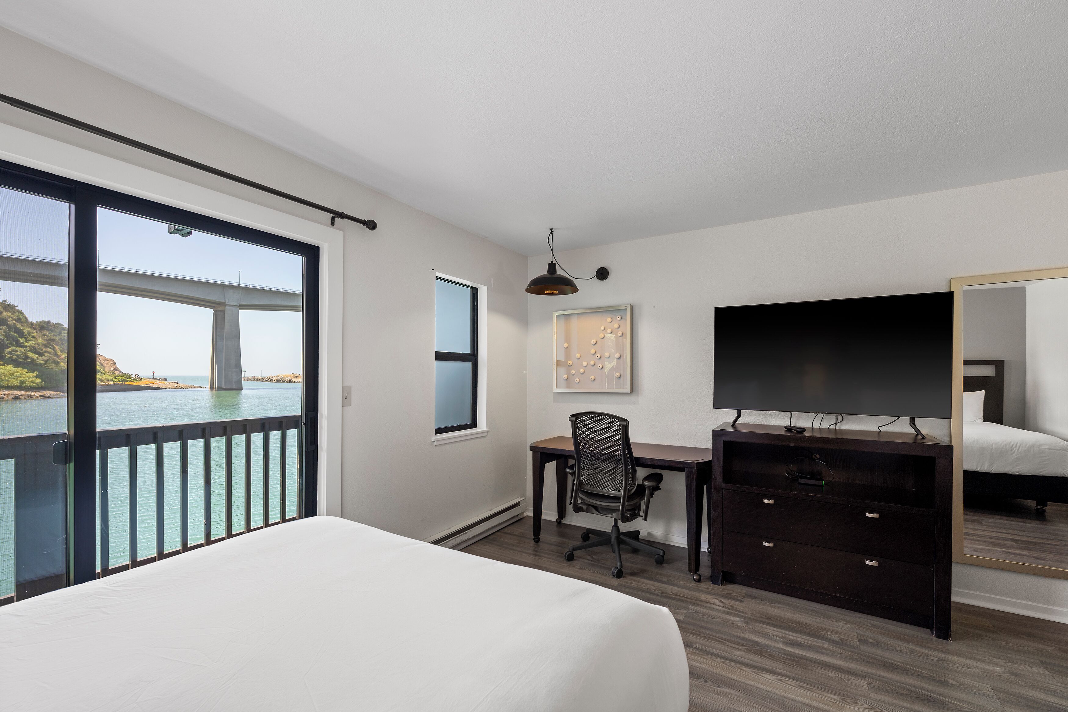 A hotel room with a large bed, a desk with a chair, a television, and a view of a bridge over water.