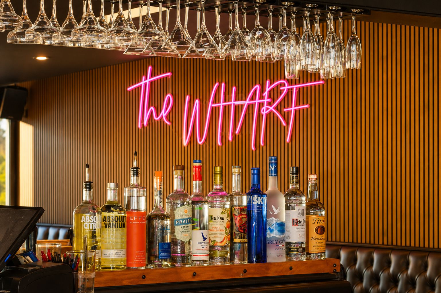 Zona de bar con un letrero de neón que dice 'the WHART' y varias botellas de licor.