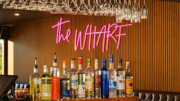 Zona de bar con un letrero de neón que dice 'the WHART' y varias botellas de licor.