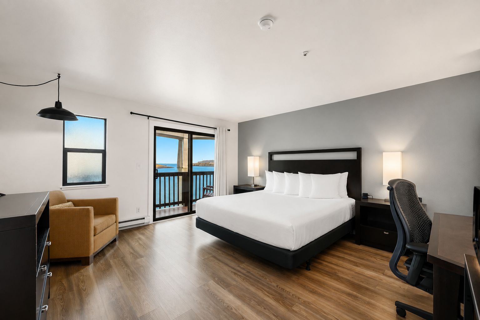 Een moderne hotelkamer met een groot bed, een bureau, een stoel en een balkon met uitzicht.