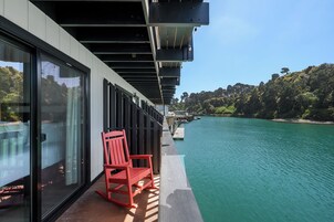 Una terraza con pared de vidrio, una mecedora roja y vistas a un río y bosque.
