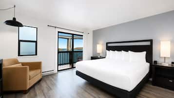 A hotel room with a large bed, a sofa, a desk, and a balcony with a view of the sea.