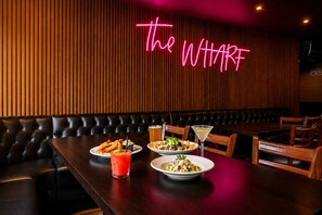 A restaurant interior with a neon sign, leather booth seating, and a table with food and drinks. - Anchor Lodge  (Fort Bragg)