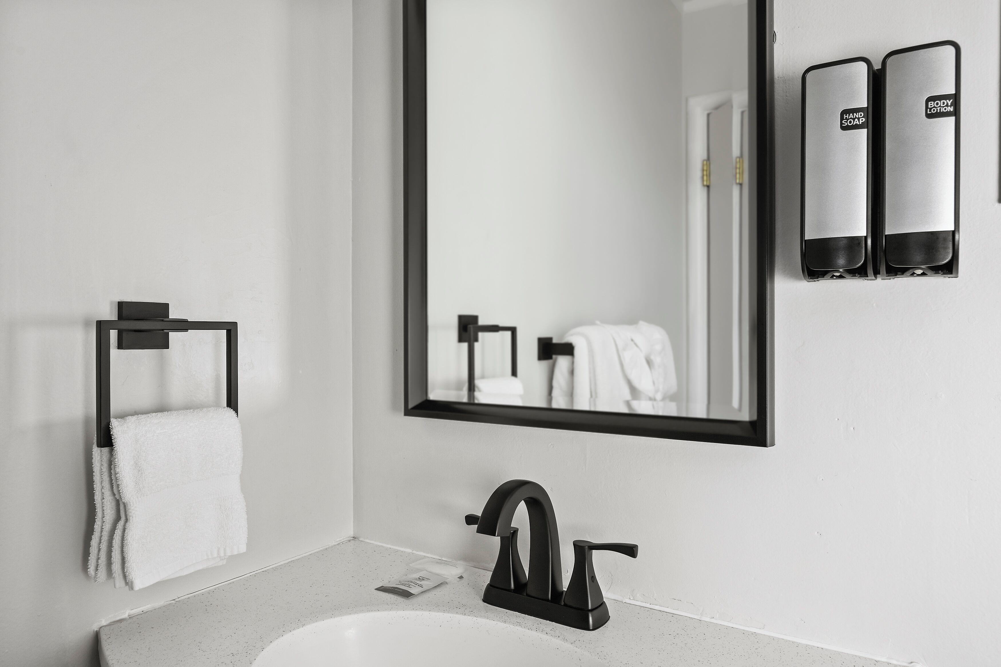 A modern bathroom with a large mirror, a black faucet, and two hand soap dispensers.
