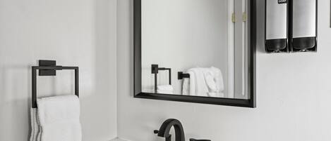 A modern bathroom with a large mirror, a black faucet, and two hand soap dispensers.