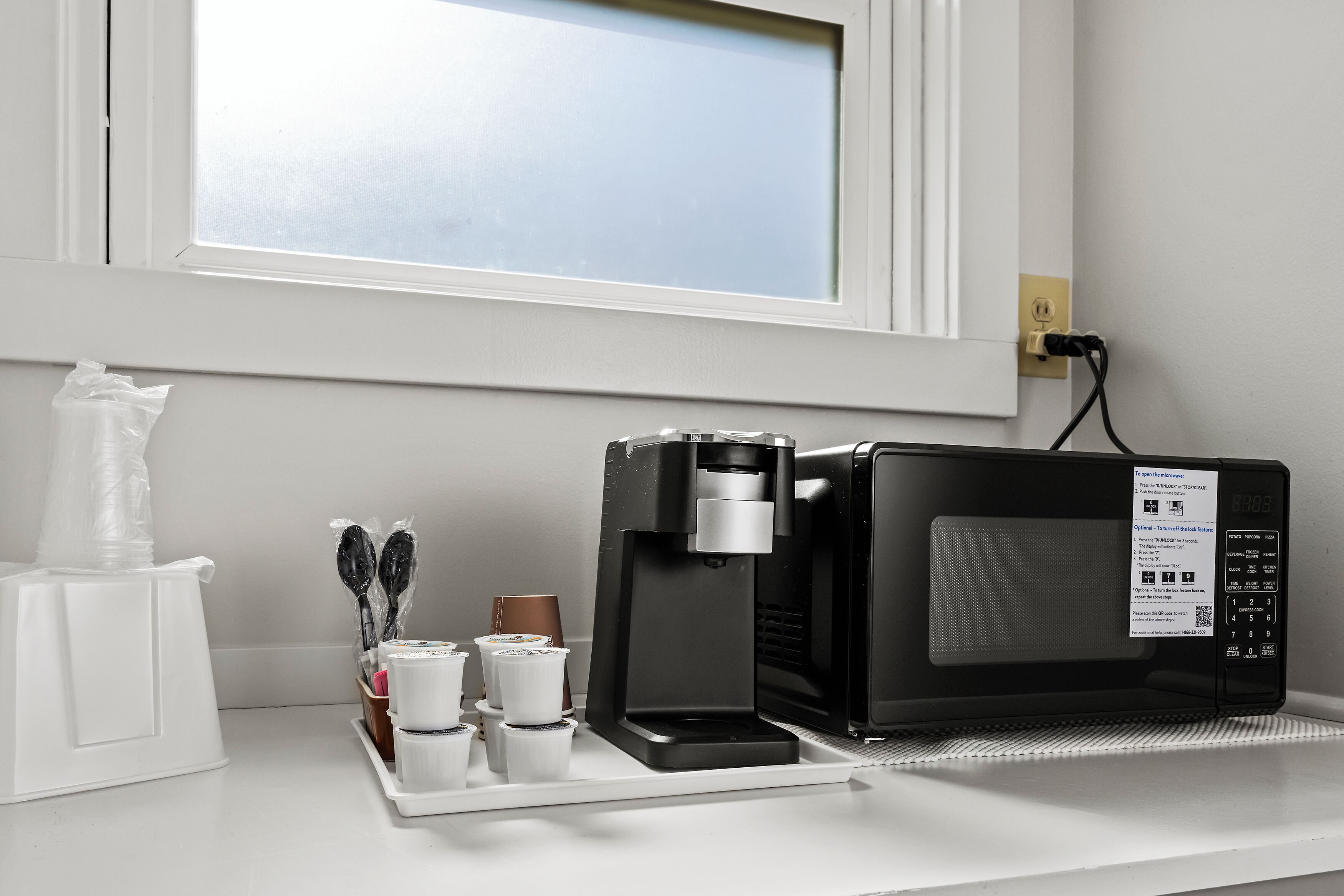 Une machine à café et un four à micro-ondes sont posés sur un plan de travail blanc, avec une fenêtre au-dessus.