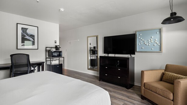 A hotel room with a bed, a desk, a chair, a television, and a mirror. - Anchor Lodge  (Fort Bragg)