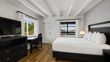 A modern hotel room with a large bed, a desk, a TV, and a balcony with a view.
