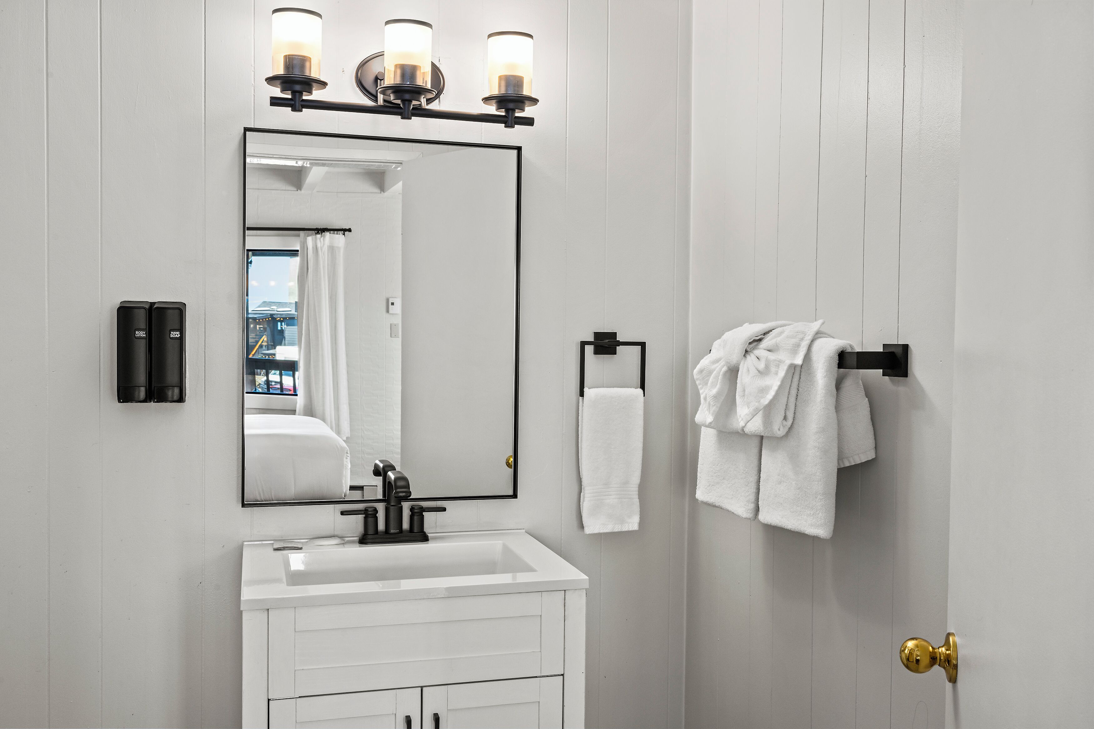 Un baño con un lavamanos blanco, un espejo y dos luces empotradas.
