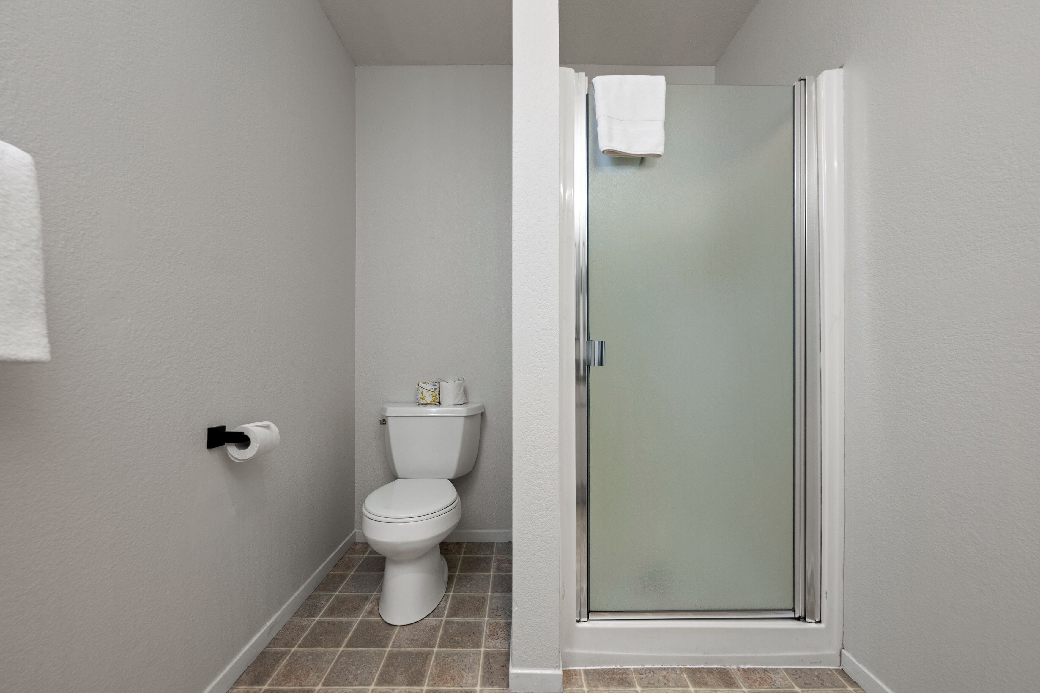 Un baño con inodoro, cabina de ducha de vidrio y un rollo de papel higiénico en la pared.