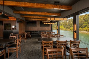 Un restaurante con mobiliario de madera, un banco acolchado negro y grandes ventanales con vistas a un lago.
