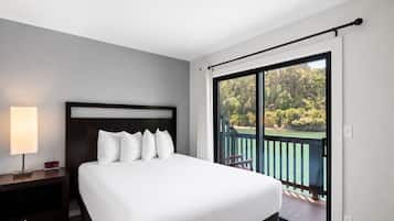 Une chambre d’hôtel avec un lit, une table de chevet, une lampe et une vue sur un balcon doté d’une balustrade.